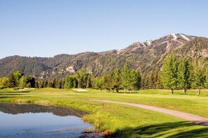 Um campo de golfe com lago, árvores e uma montanha ao fundo.