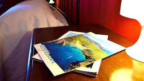 Una habitación de hotel con una cama, una mesita de noche con una lámpara y un folleto sobre la mesita.