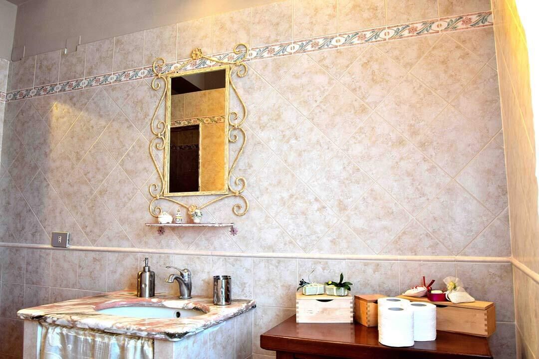 Ein Badezimmer mit Marmorwaschbecken, einem spiegel mit goldener Rahmung und Pflegeprodukten auf einem Holzboden.