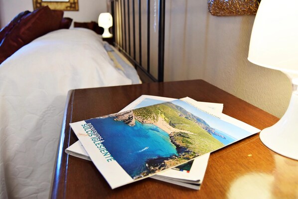 Habitación de hotel con una cama bien hecha, una mesita de noche de madera con una lámpara y un folleto sobre la mesita.