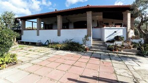 Una casa de dos pisos con un porche cubierto, entrada empedrada y plantas en macetas.