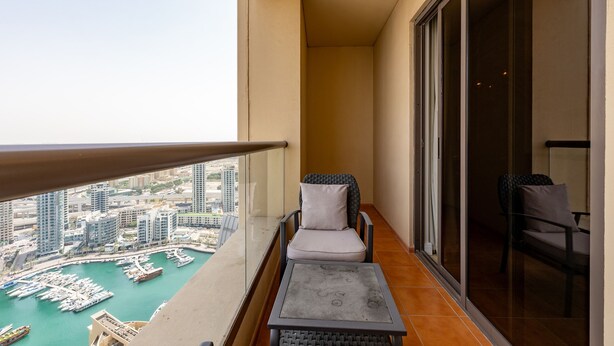 Een balkon met uitzicht op een jachthaven en gebouwen. Er staan twee stoelen en een klein tafeltje.