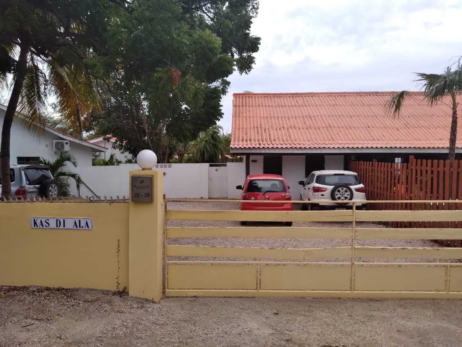 A gated entrance with a sign reading "KAS DI ALA" and a building with a red-tiled roof.