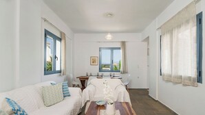 Et moderne, godt oplyst rum med et træspisebord, hvidt møbel og udsigt til det fri via store vinduer.
