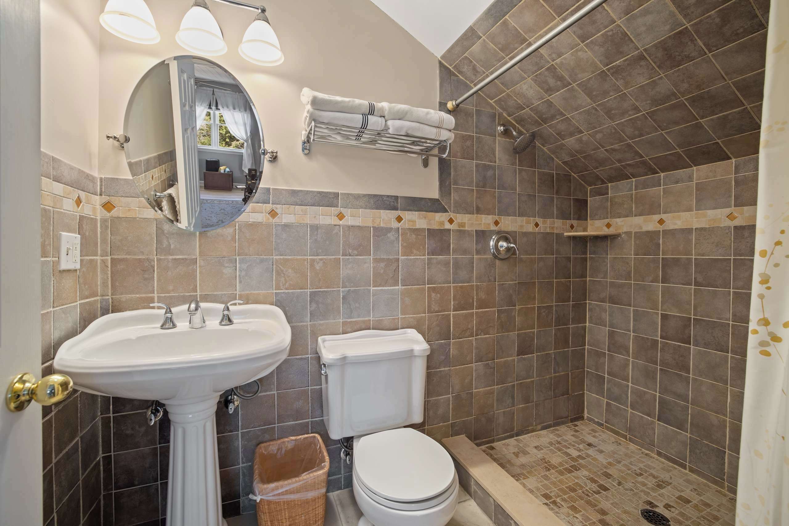 Une salle de bain comprenant un lavabo sur colonne, des toilettes, une douche avec une porte en verre et un miroir avec éclairage intégré.