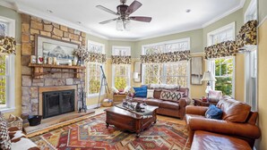 A living room with a stone fireplace, leather sofas, a patterned rug, and large windows with curtains. - Forest Retreat | 25 Min to Stratton (Windham)