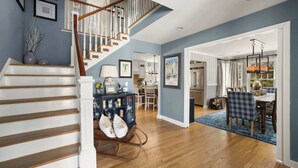 A spacious living area with a wooden staircase, a dining table with chairs, and a kitchen in the background. - Forest Retreat | 25 Min to Stratton (Windham)