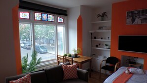 Un salon avec un canapé, une table et un téléviseur. Il y a une fenêtre donnant sur la rue.