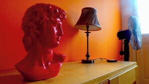 Un buste posé sur une table en bois, avec une lampe et un ventilateur.