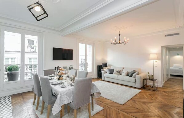 A modern living room with a dining area, a sofa, a TV, and a chandelier.