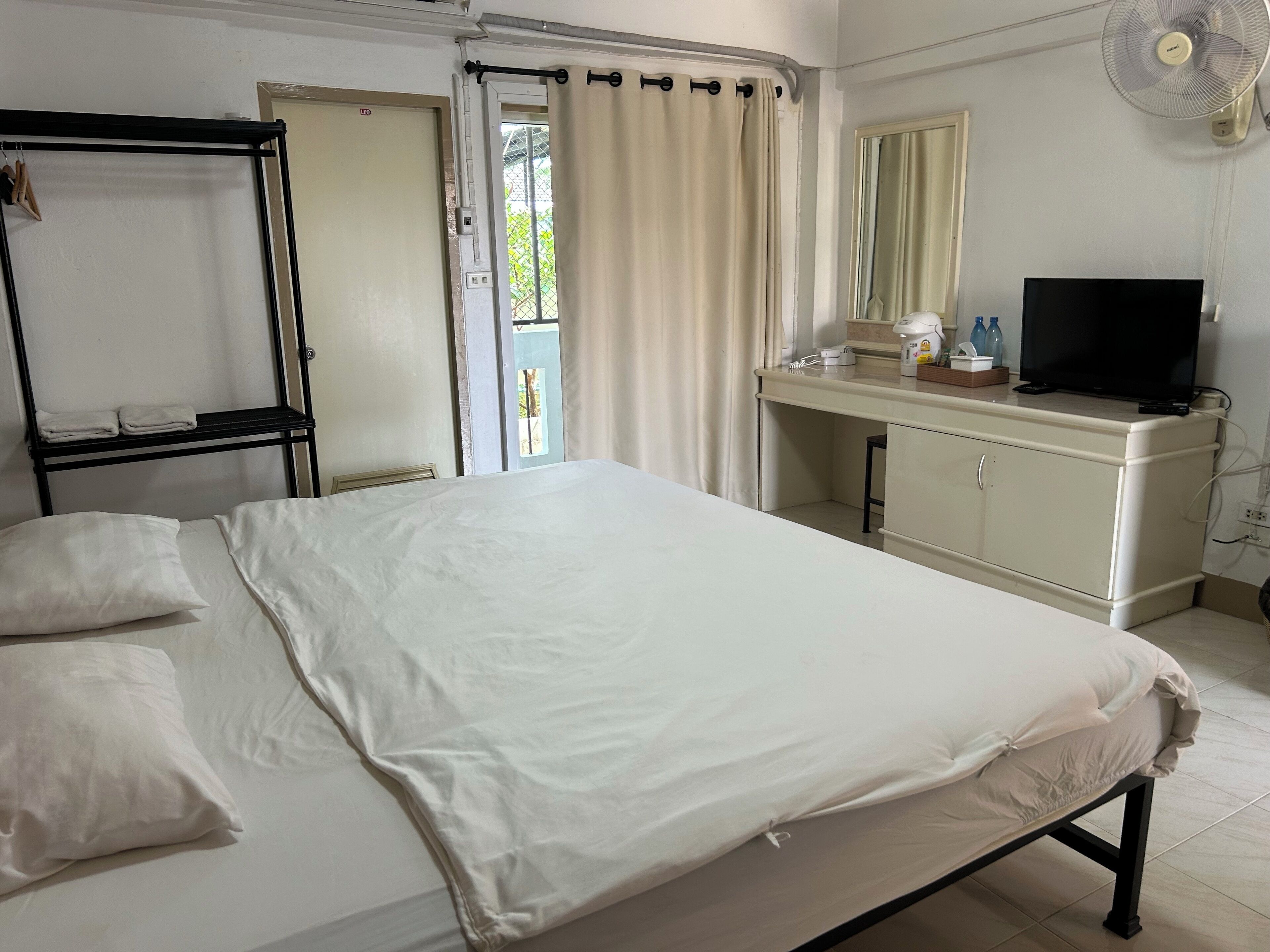 Une chambre d’hôtel avec un lit, un bureau avec une télévision, un miroir et une fenêtre avec des rideaux.