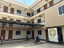 Un edificio residencial de varios pisos con balcones numerados y un estacionamiento techado.