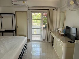 Una habitación de hotel con una cama, un escritorio con televisor, un ventilador y aire acondicionado.