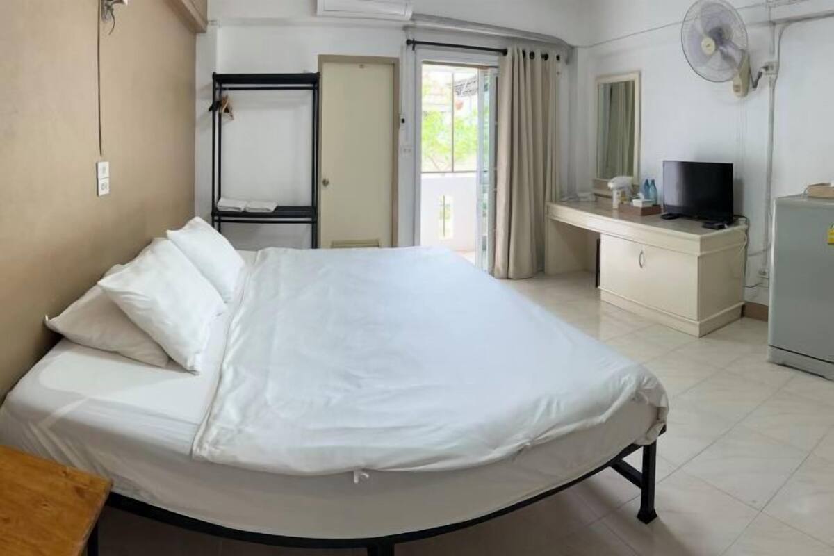 Una habitación de hotel con cama, escritorio, televisor, ventilador y armario.