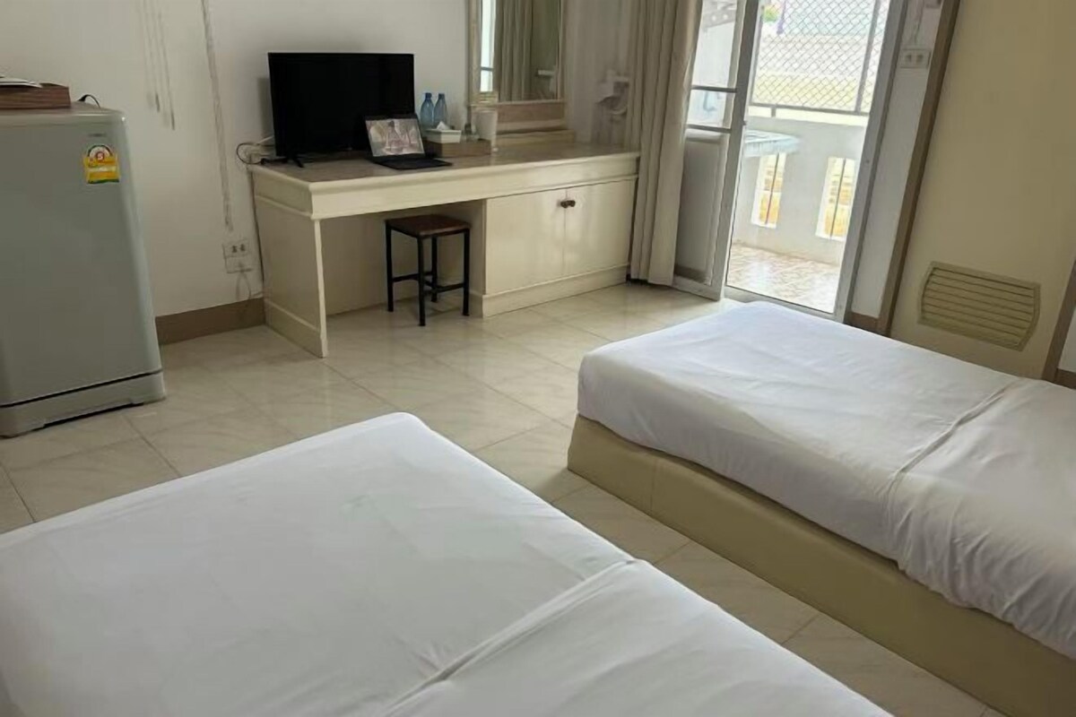 A hotel room with two beds, a desk with a television, a refrigerator, and a window with a view.