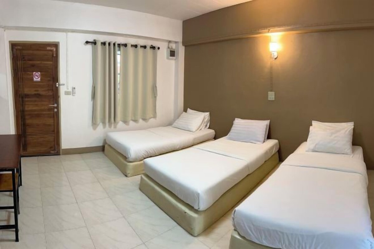 A hotel room with two single beds, a wooden door, a curtain, a wall-mounted light, and a small table.