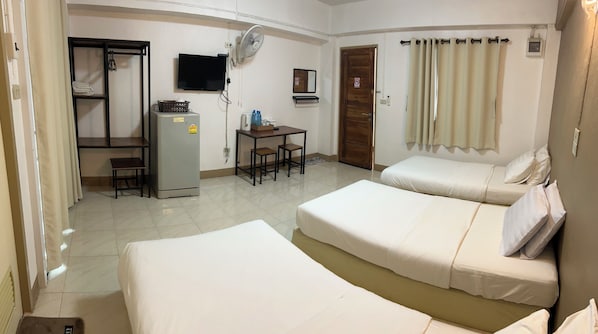 A hotel room with two beds, a desk with chairs, a refrigerator, a TV, and a door with a wooden panel. - Phuviewplace (Chiang Kham)