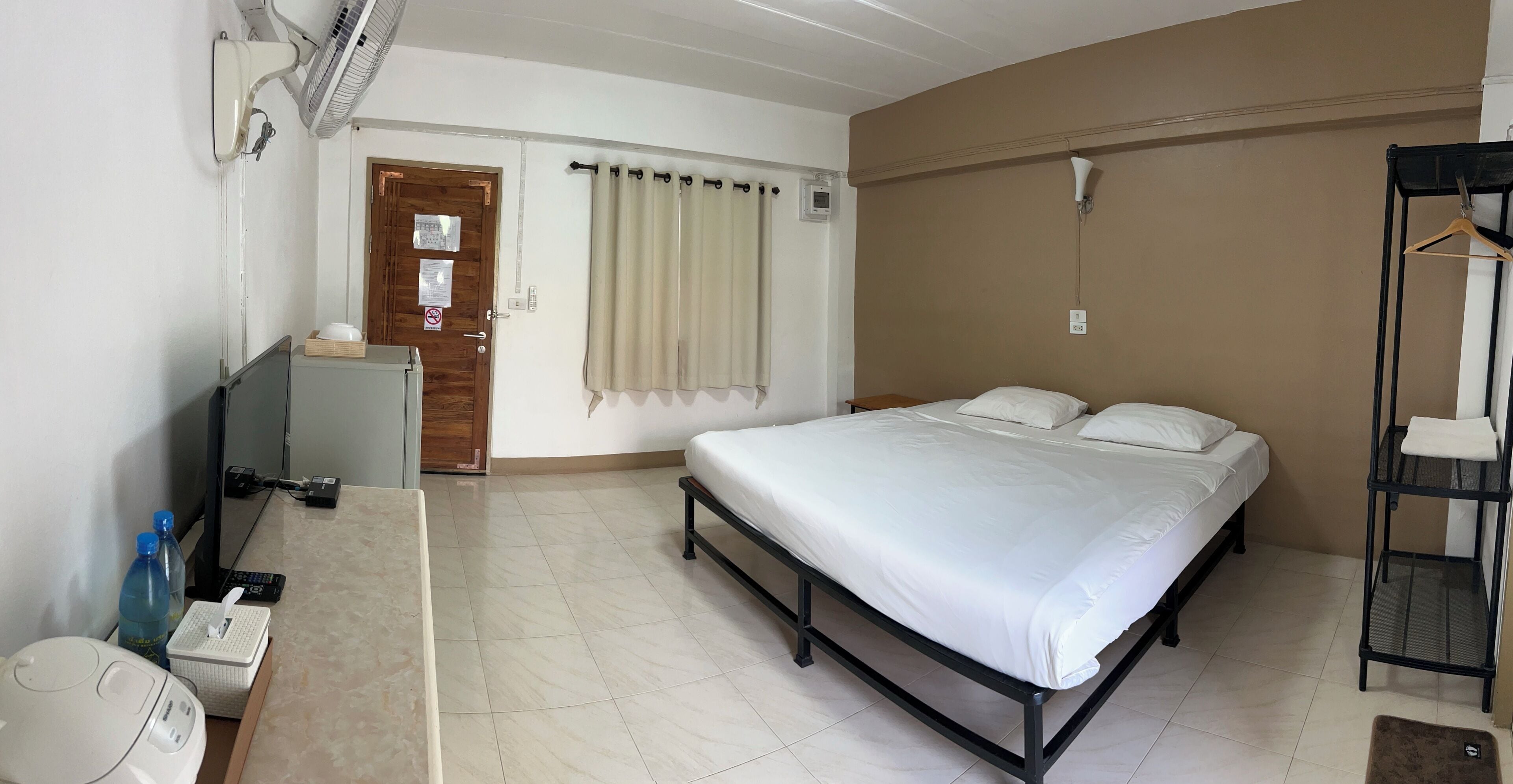A bedroom with a bed, a desk with a computer, a chair, a hanging light fixture, and a door.