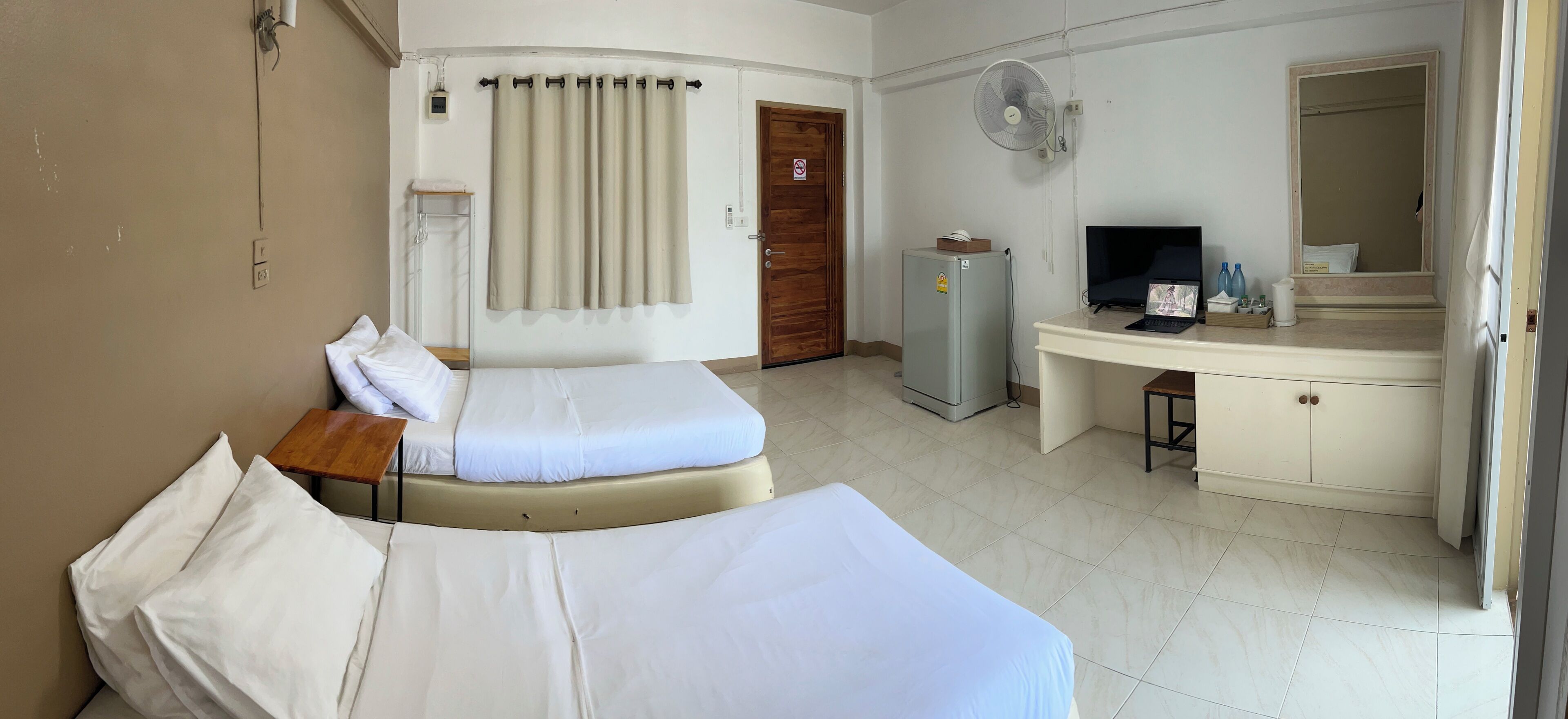 Una camera d'albergo con due letti, una scrivania, un frigorifero, una televisione e uno specchio.