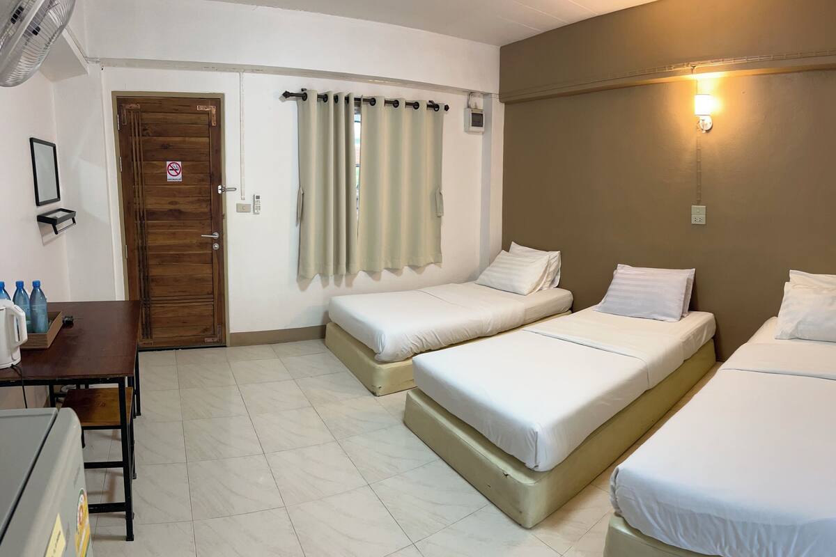 Habitación de hotel con dos camas individuales, una puerta de madera, una mesita con botellas de agua y una lámpara fijada a la pared.