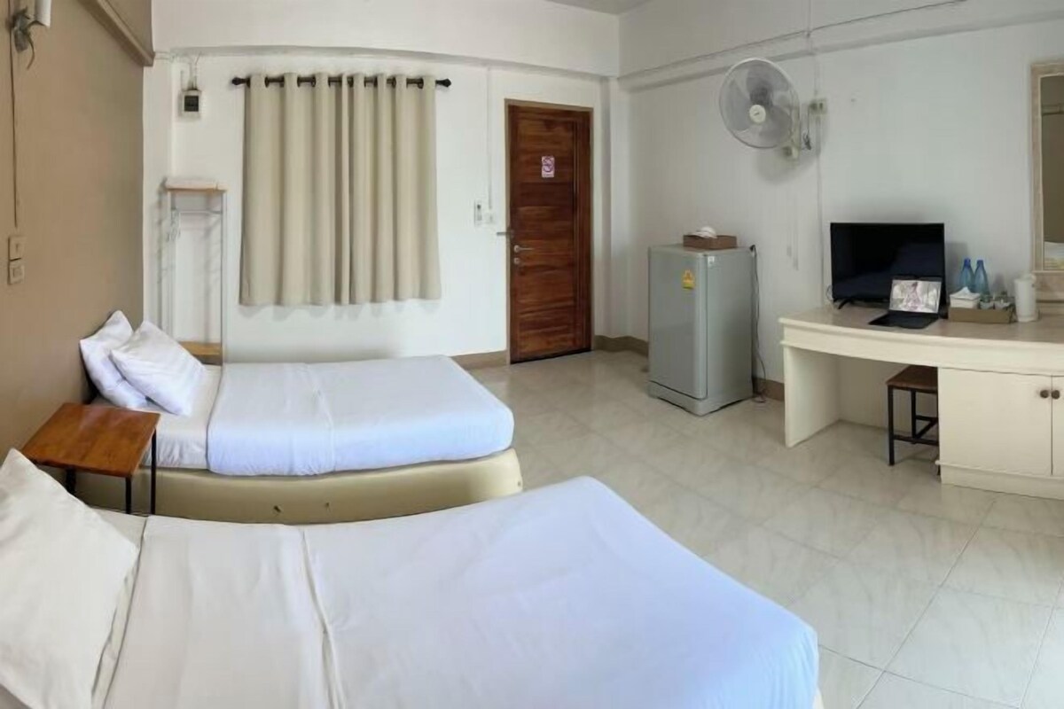 A hotel room with two beds, a desk, a television, a refrigerator, and a curtain.