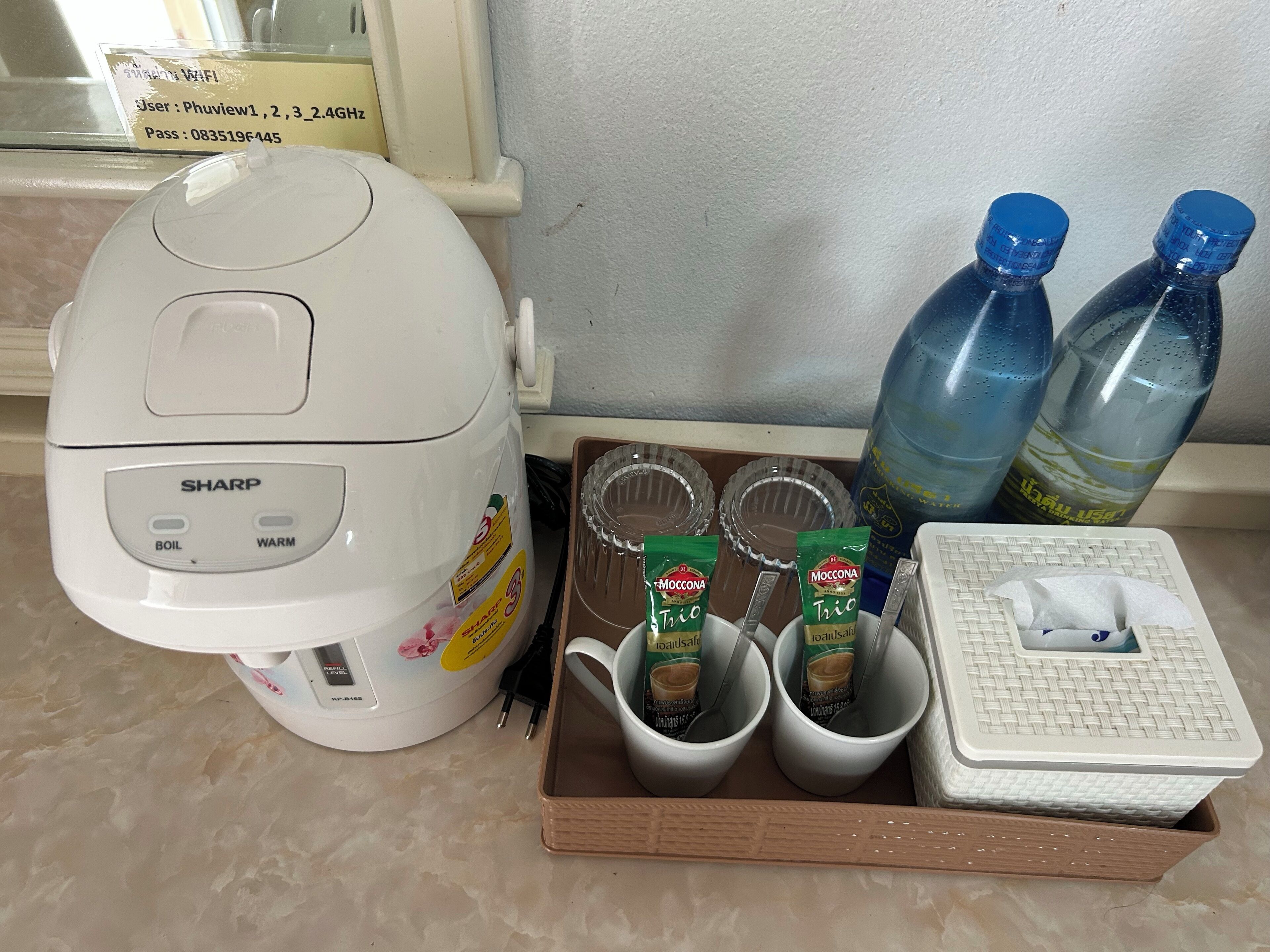 Eine Küchenzeile mit Kaffeemaschine, zwei Wasserflaschen, einer Kapselbox und einem Taschentuchspender.