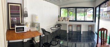 Cocina compacta con microondas, tostadora y cafetera sobre una mesa de madera. Hay una mesita redonda con sillas y una ventana con vistas al exterior.