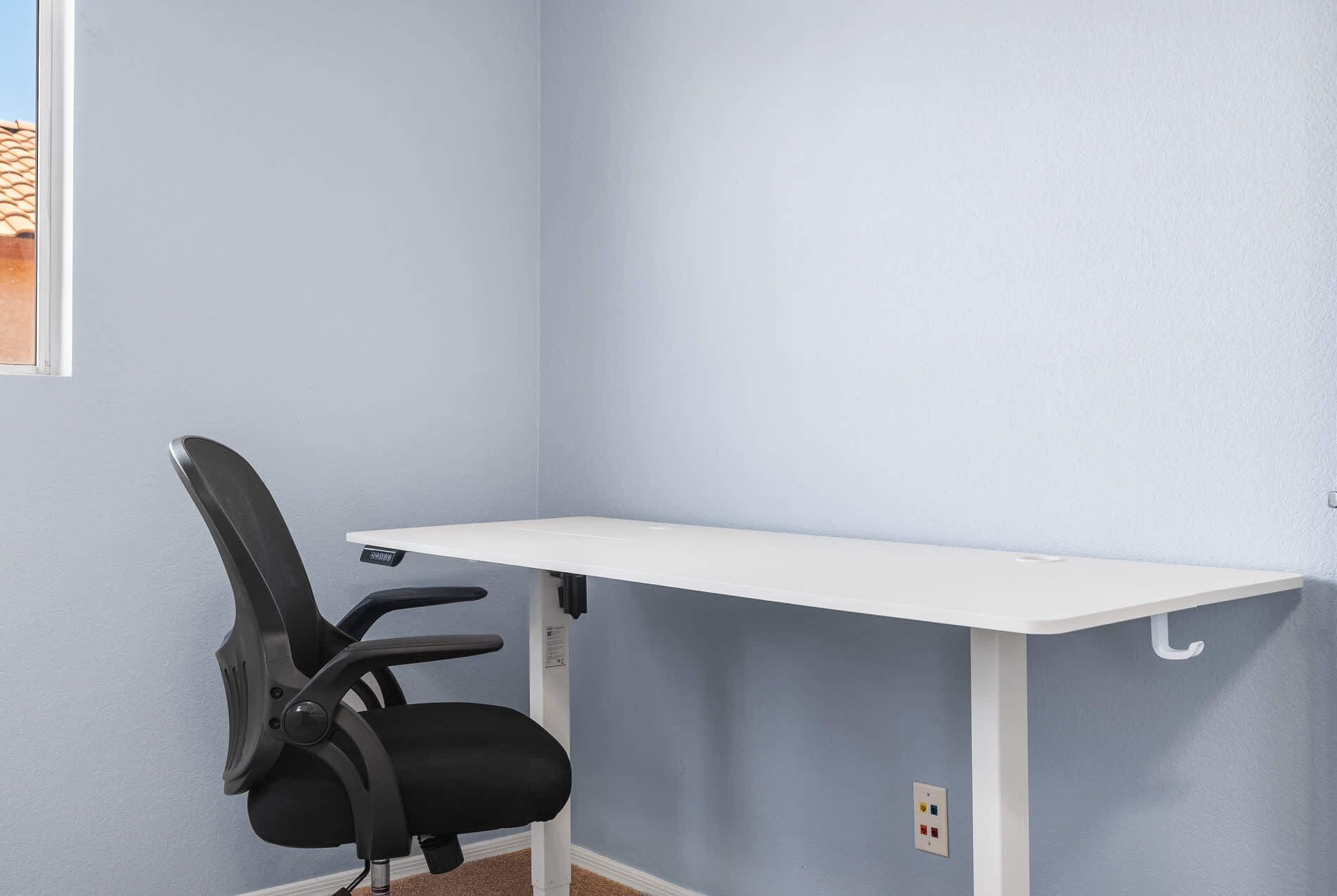 A corner desk with a black office chair, a white desk, and a blue wall.