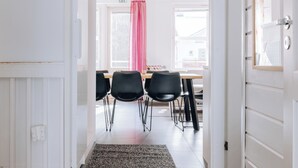 A hallway leading to a dining area with a table and chairs, a red curtain, and a view of the outside.