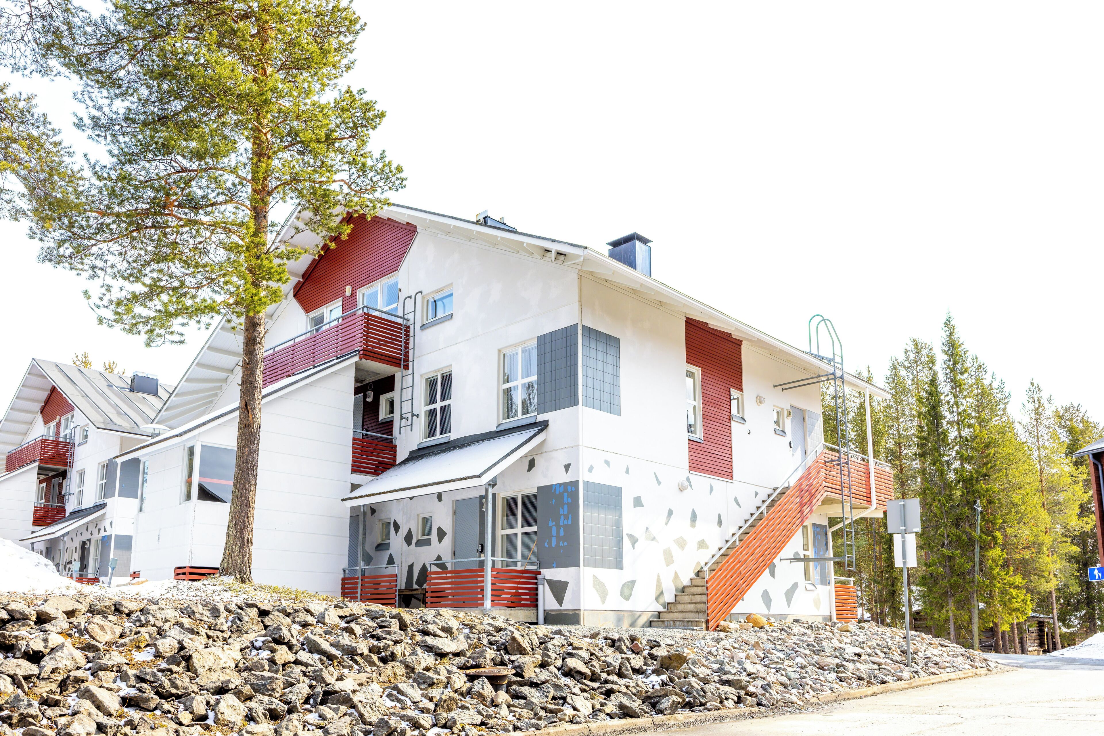 A modern multi-story building with a white facade, red accents, and a stone base.