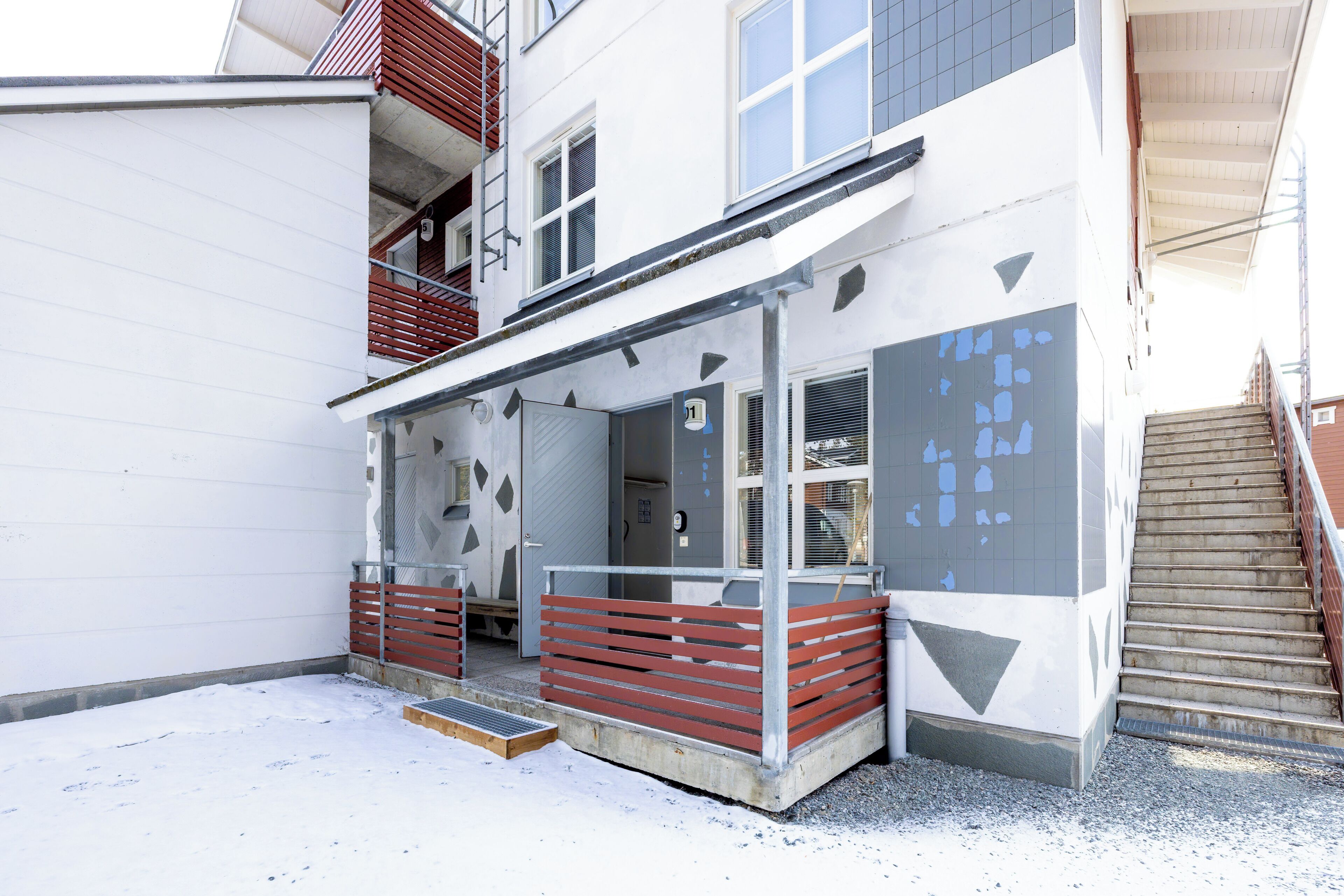 Un edificio con un espacio exterior techado, una escalera y una puerta con el número 1.