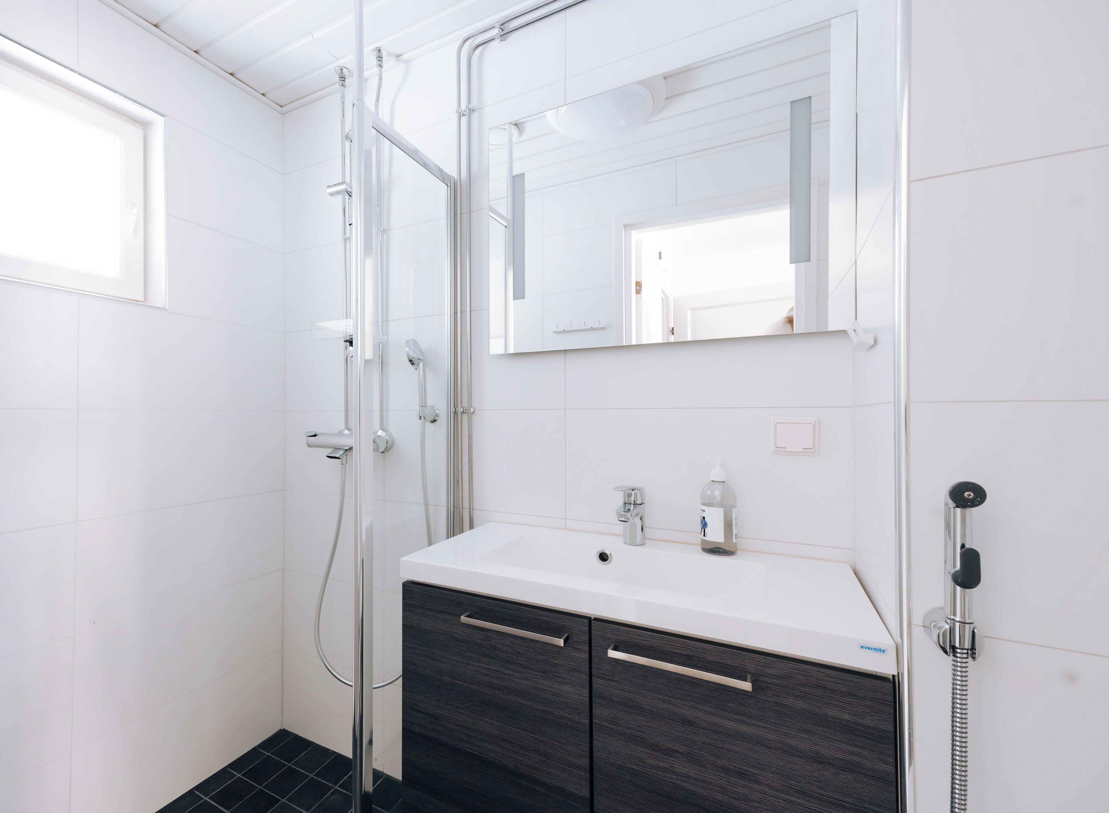 Une salle de bain moderne avec une douche à l’italienne en verre, un lavabo blanc avec un miroir au-dessus et des meubles en bois foncé en dessous.
