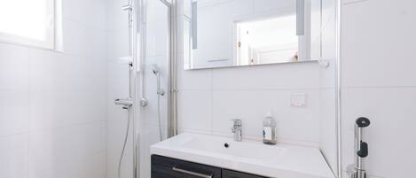 Une salle de bain moderne avec une douche à l’italienne en verre, un lavabo blanc avec un miroir au-dessus et des meubles en bois foncé en dessous.