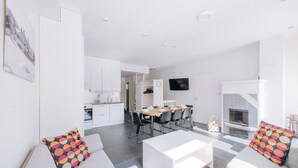 A modern living room with a sofa, coffee table, and a fireplace. There is a dining area with a table and chairs in the background.