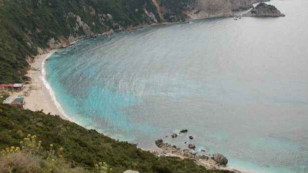 Eine Küstenlandschaft mit Strand, Felsenformationen und einer kleinen Siedlung mit Gebäuden.