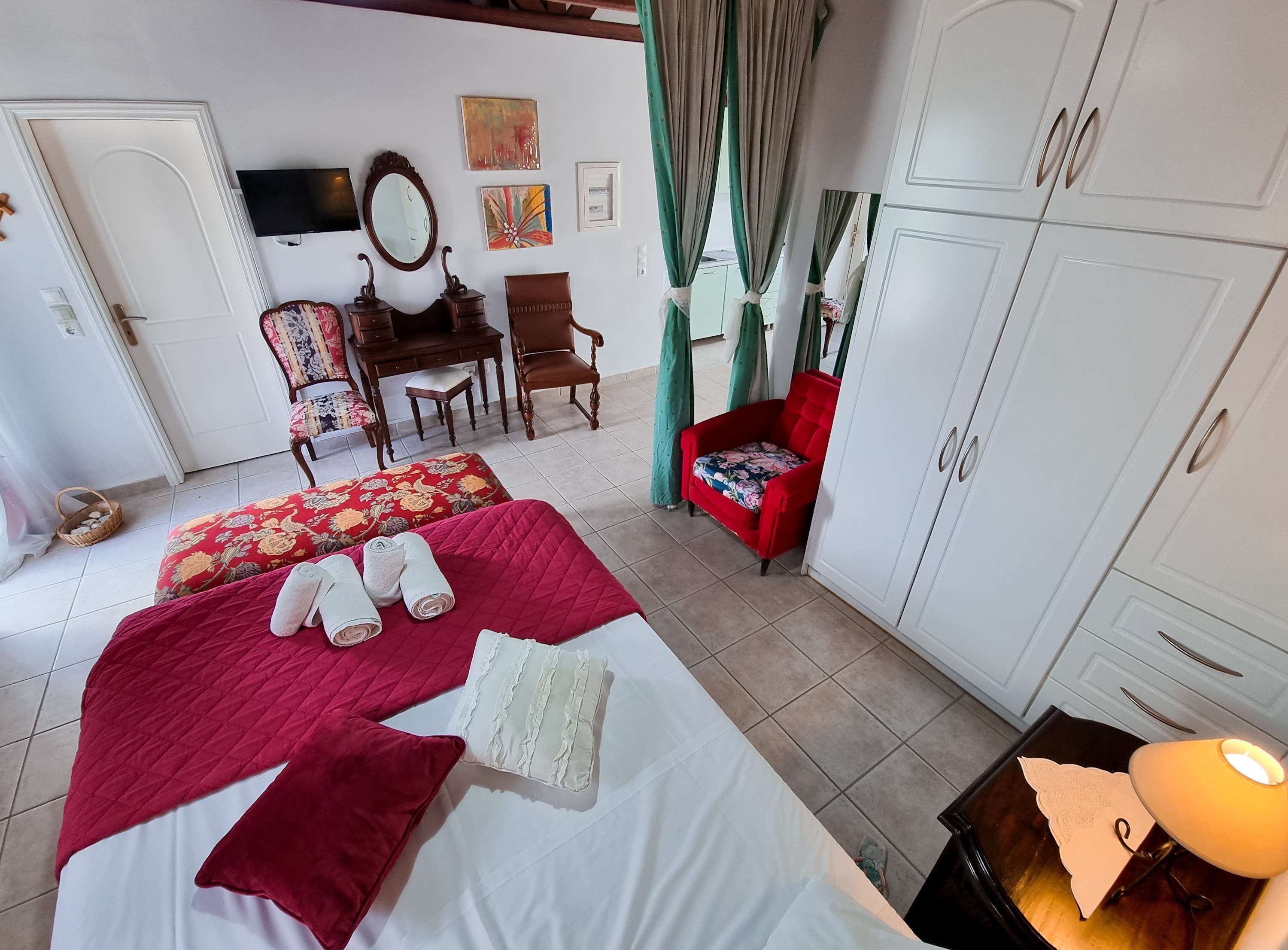 Habitación de hotel con cama, escritorio, silla, armario y televisión en la pared.