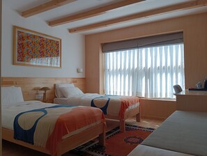 A hotel room with two beds, a large window with curtains, a wooden ceiling, and a colorful painting on the wall. - Mountain Lodges of Nepal Chame (Chame)