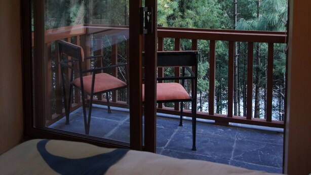 Ein Zimmer mit einem Bett, einem Fenster mit Balkonblick und einem Sessel.