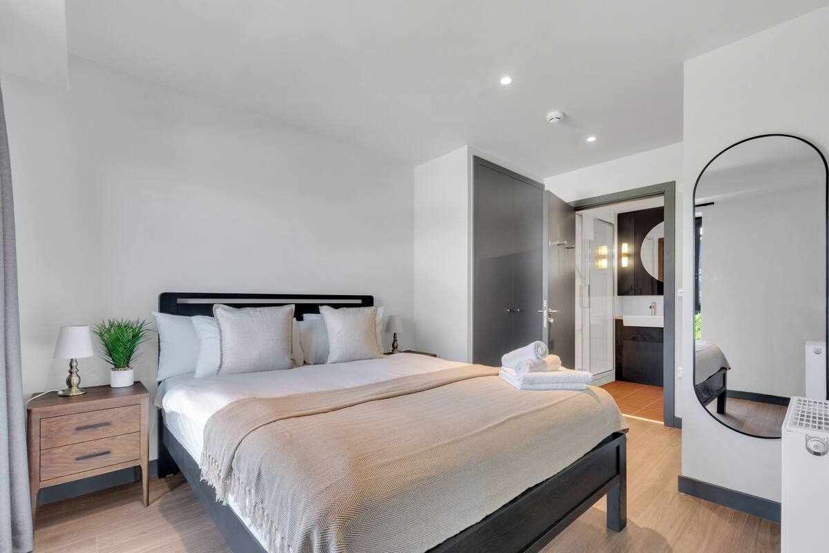 A modern bedroom with a bed, bedside table, lamp, and a mirror.