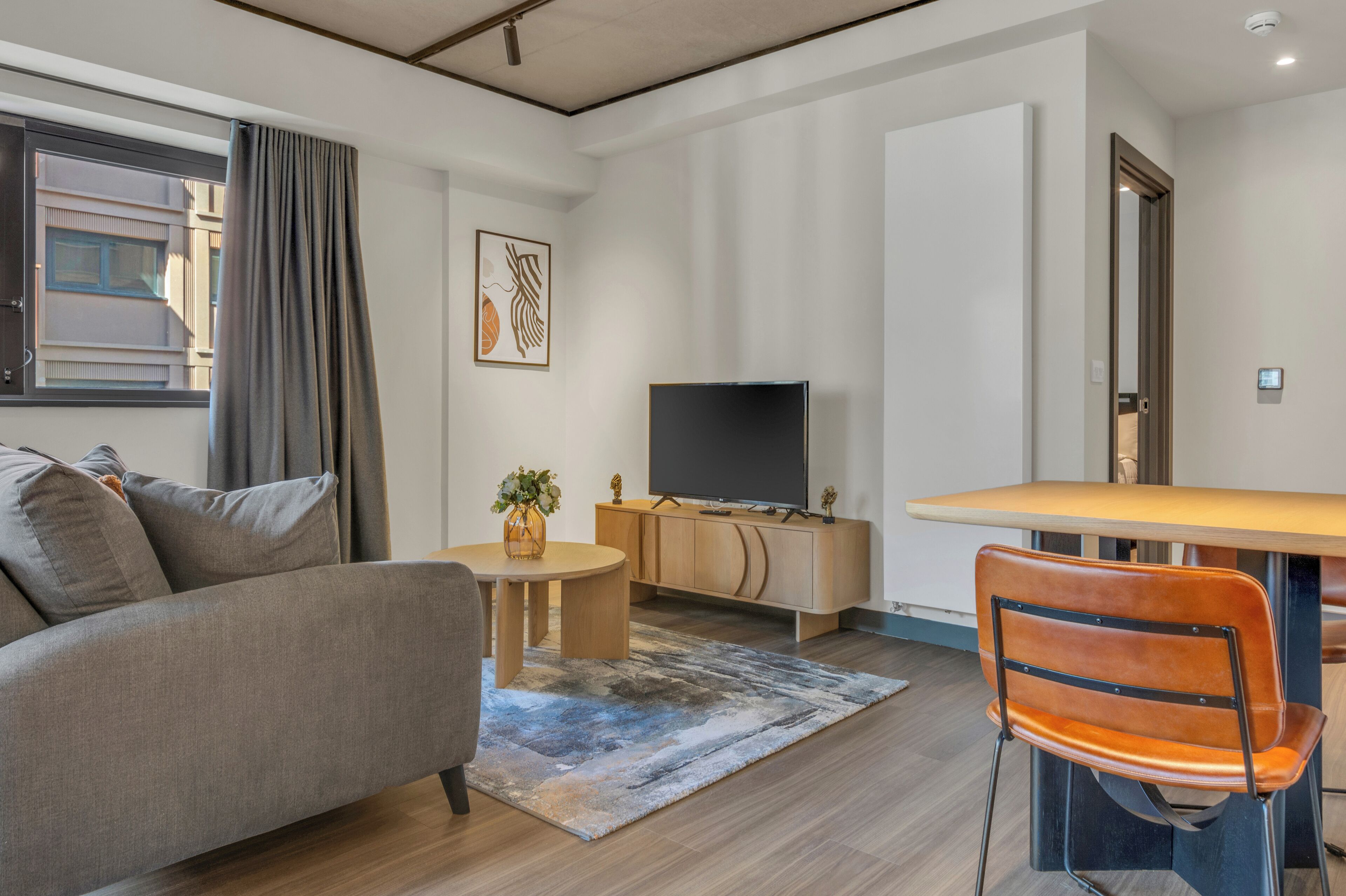 A modern living room with a sofa, a dining table, a TV, and a chair.