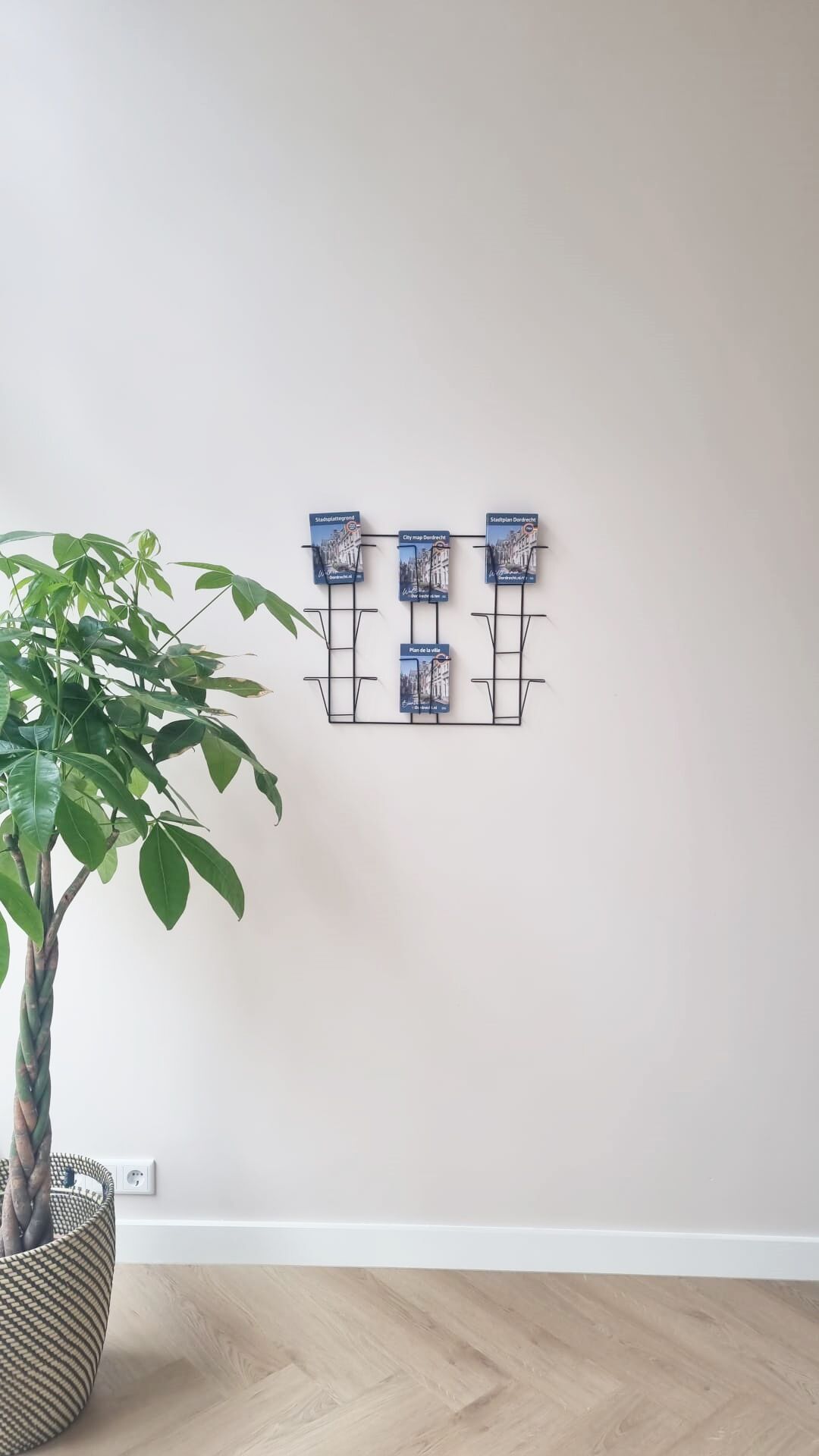 Uma prateleira metálica fixada na parede com quatro mapas de cidades, uma planta em vaso e uma tomada.