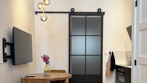 Una cocina moderna con una puerta corredera negra, un televisor montado y una mesa de comedor de madera con sillas.