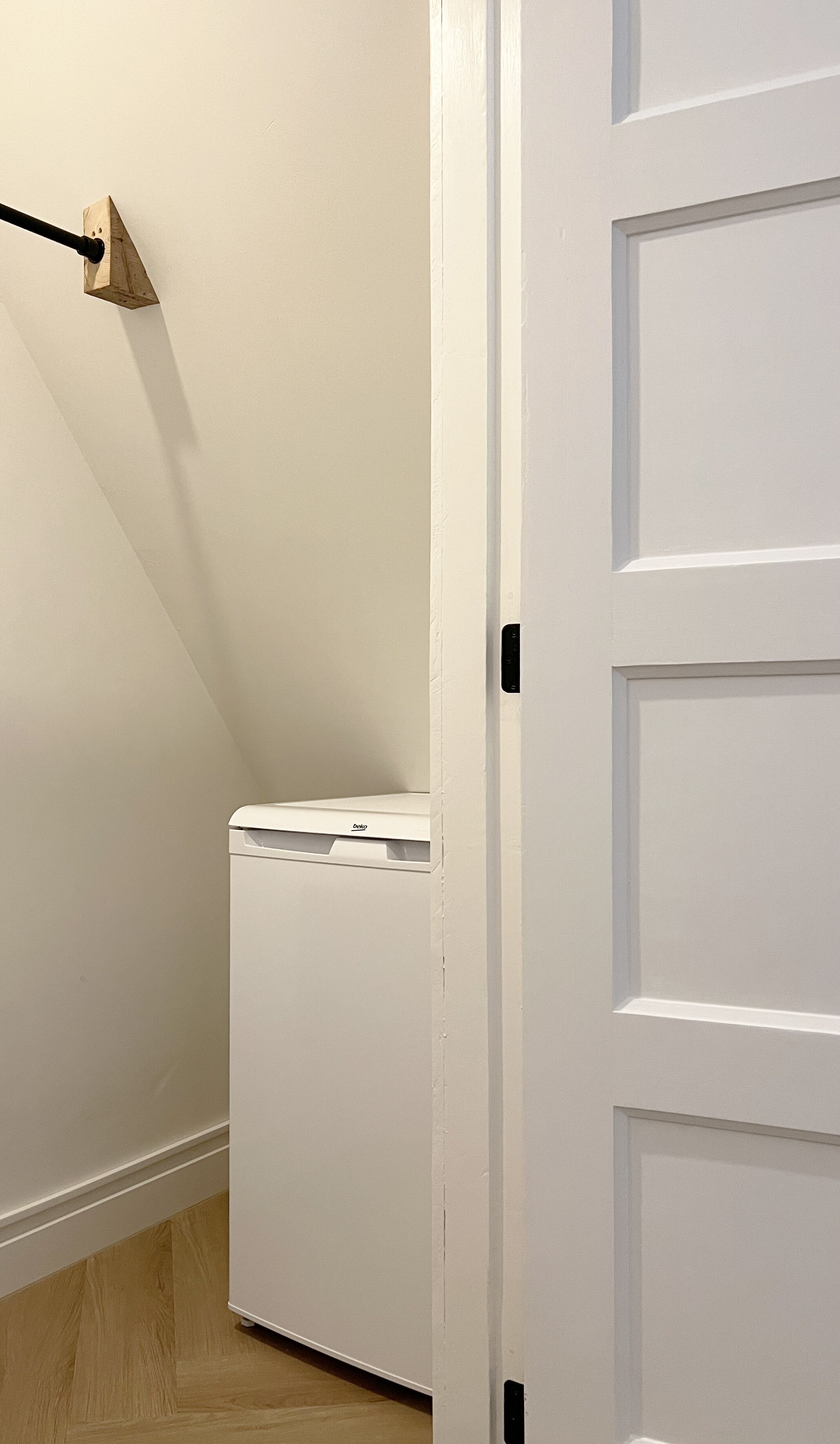 Une buanderie avec un lave-linge blanc, une étagère en bois et une porte dotée d’une poignée.