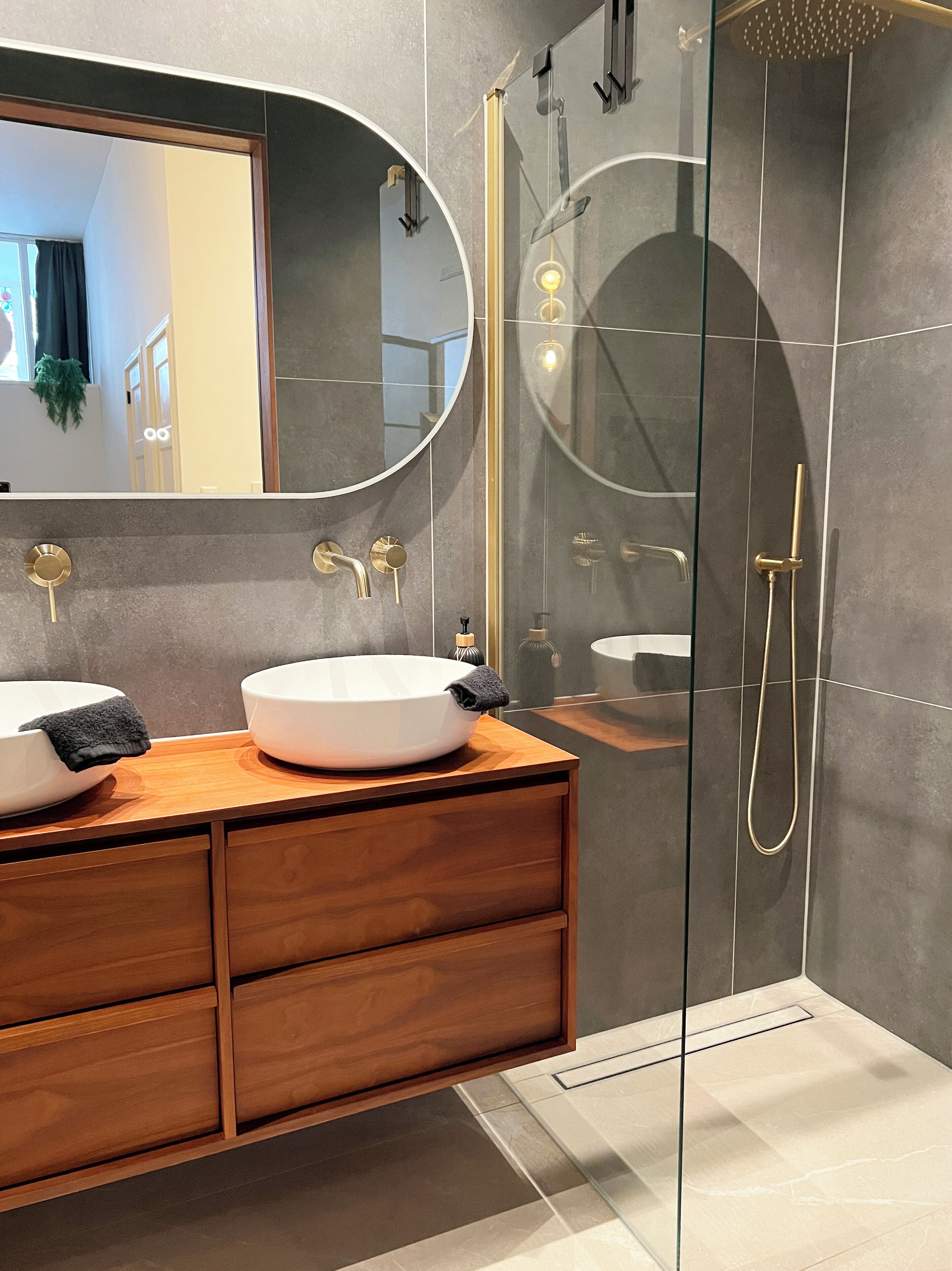 Un baño moderno con dos lavamanos, un espejo grande y una ducha con cerramiento de vidrio.
