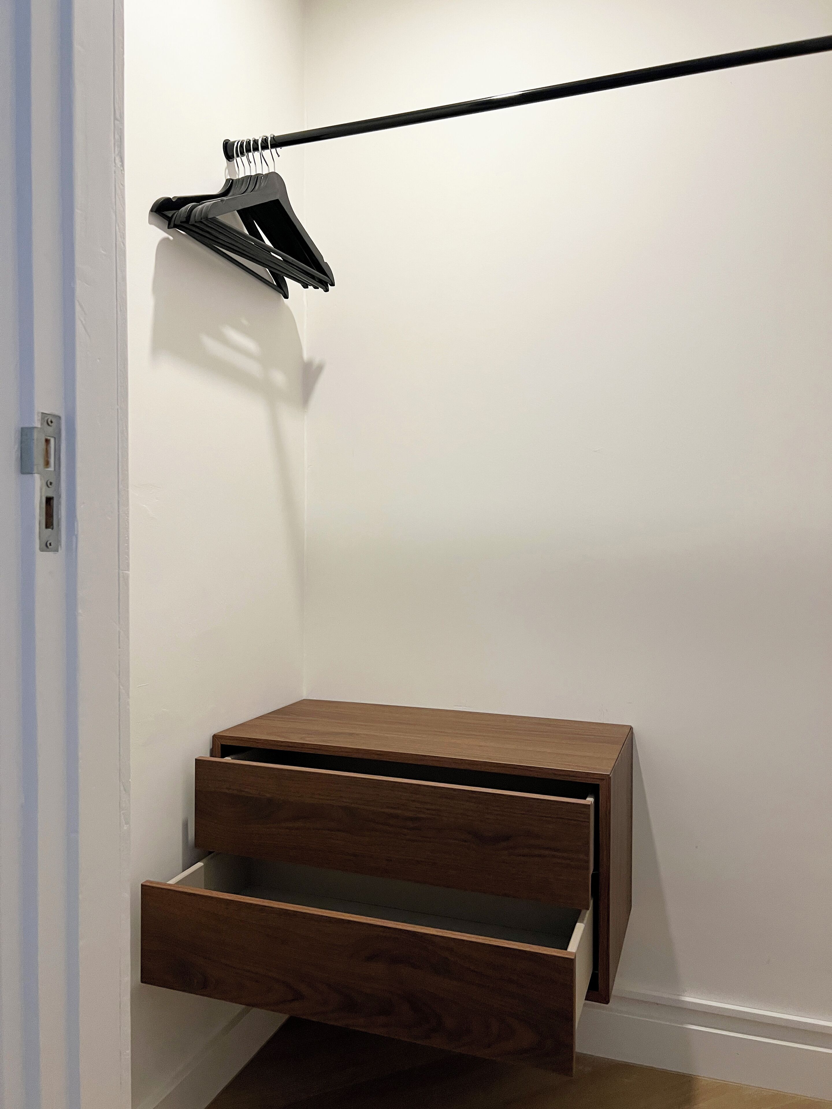 A corner closet with a wooden bench and a hanging rack.