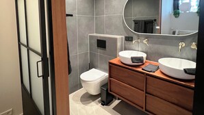 Un baño moderno con inodoro, dos lavamanos, un espejo y un mueble de tocador de madera.