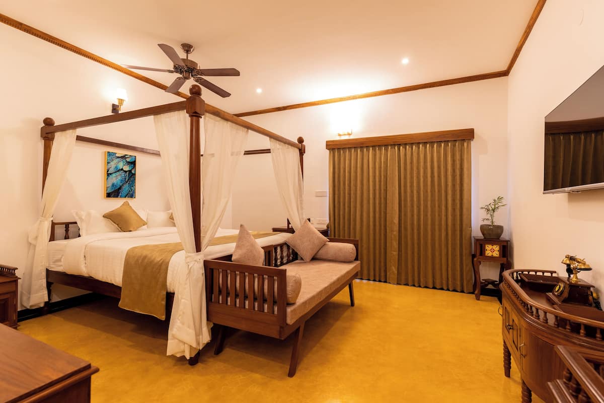 A four-poster canopy bed with a ceiling fan, a sofa, a bedside table, and a small cabinet.