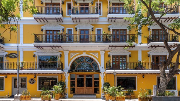 A multi-story hotel with a yellow facade, balconies with black railings, and a central entrance with a large arched doorway. - La Moon Puducherry (Puducherry)