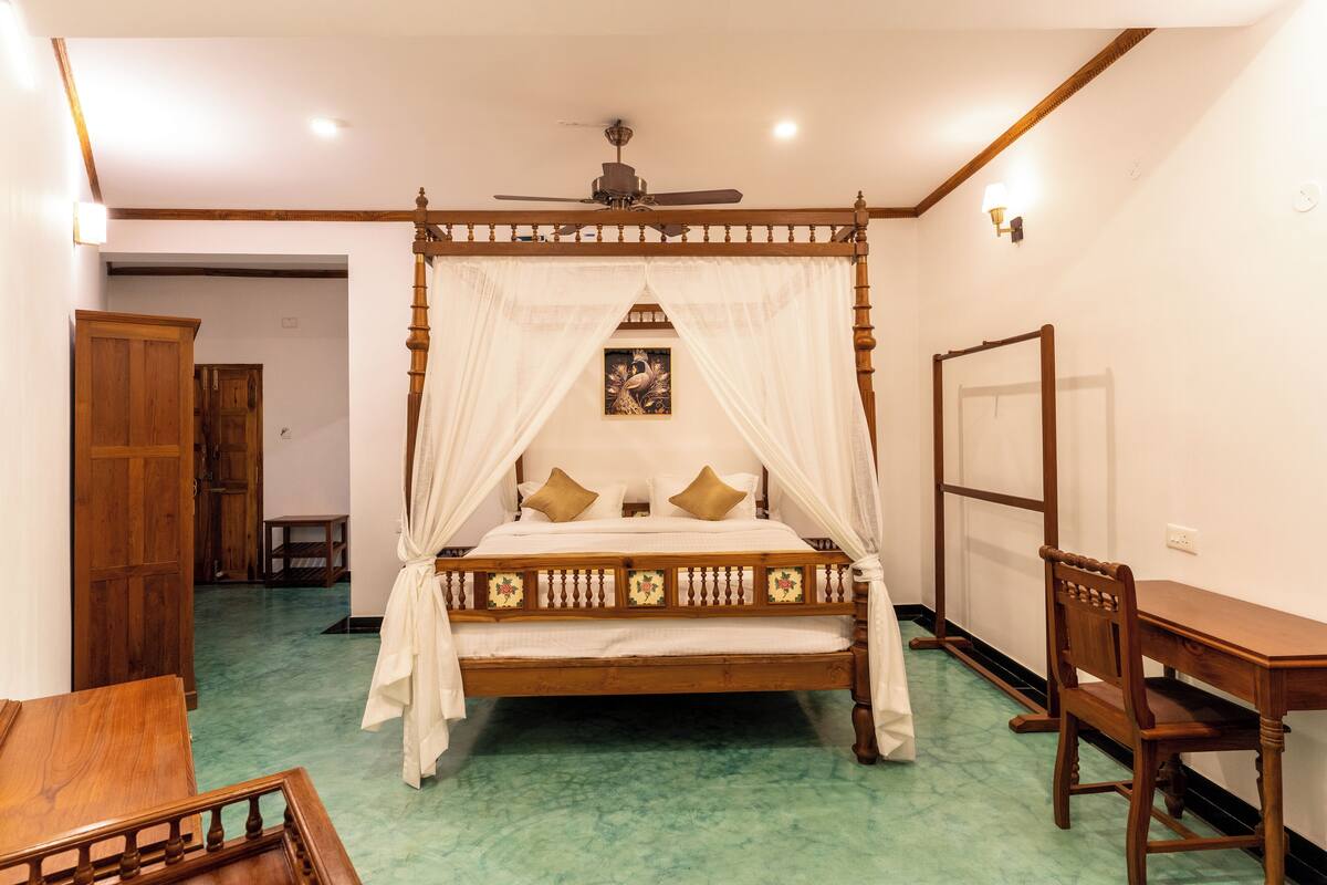 A four-poster bed with a canopy, a wooden desk, and a chair in a room with a green carpet.