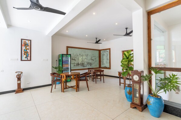 A spacious room with a high ceiling, ceiling fans, a large map on the wall, wooden furniture, and potted plants. - La Moon Puducherry (Puducherry)